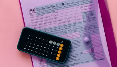 Tax form 1040 with a calculator on a pink background, highlighting finance and accounting themes.