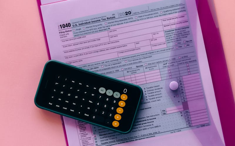 Tax form 1040 with a calculator on a pink background, highlighting finance and accounting themes.